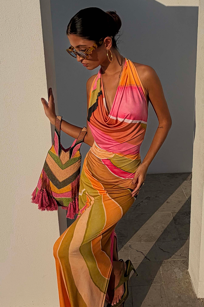 Green Abstract Sabine Dress in a multicoloured jersey with a cowl halter neck, styled with a beaded bag.