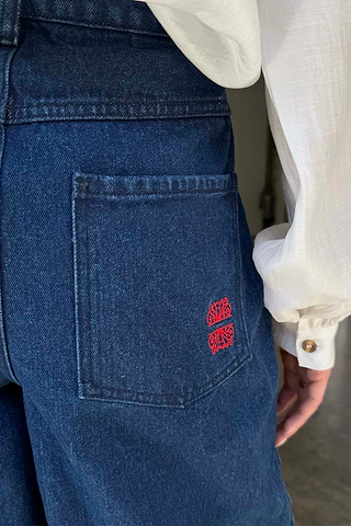 Blue Denim Pallazzo Jan Jean back pocket detail with a red embroidered logo and white shirt sleeve.