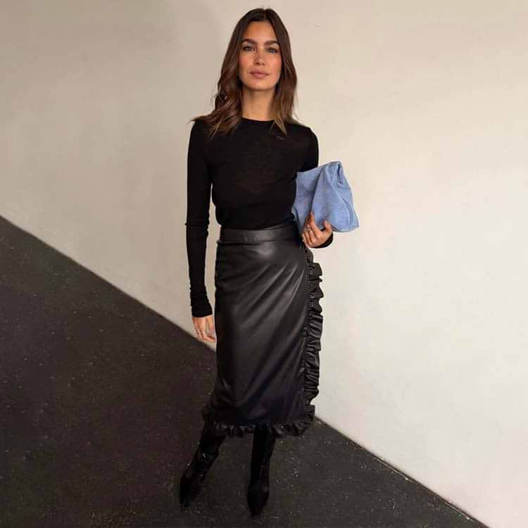 Black Vegan Leather Ruffle Jaspre Skirt with side ruffle detailing, styled with a long-sleeve top and blue clutch.