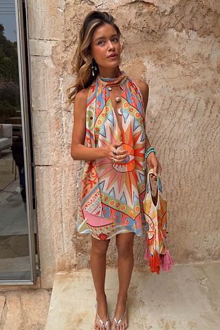Dolce Vita Josie Mini Dress in sunset tones featuring an iconic eye motif and scarf halterneck.