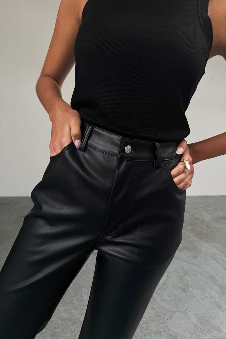 High-waisted Black Vegan Leather Trouser with front pockets, styled with a black ribbed tank top.