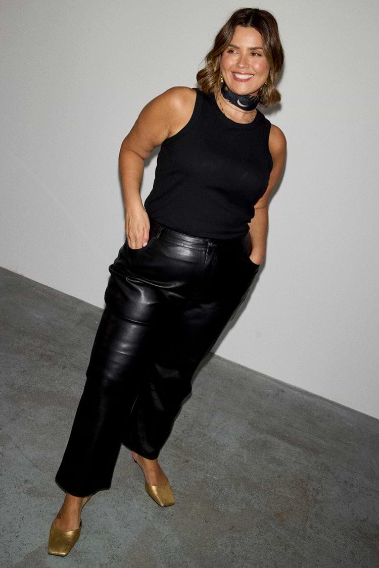 Black Vegan Leather Trousers featuring a straight-leg fit, styled with a black tank top and gold mules.