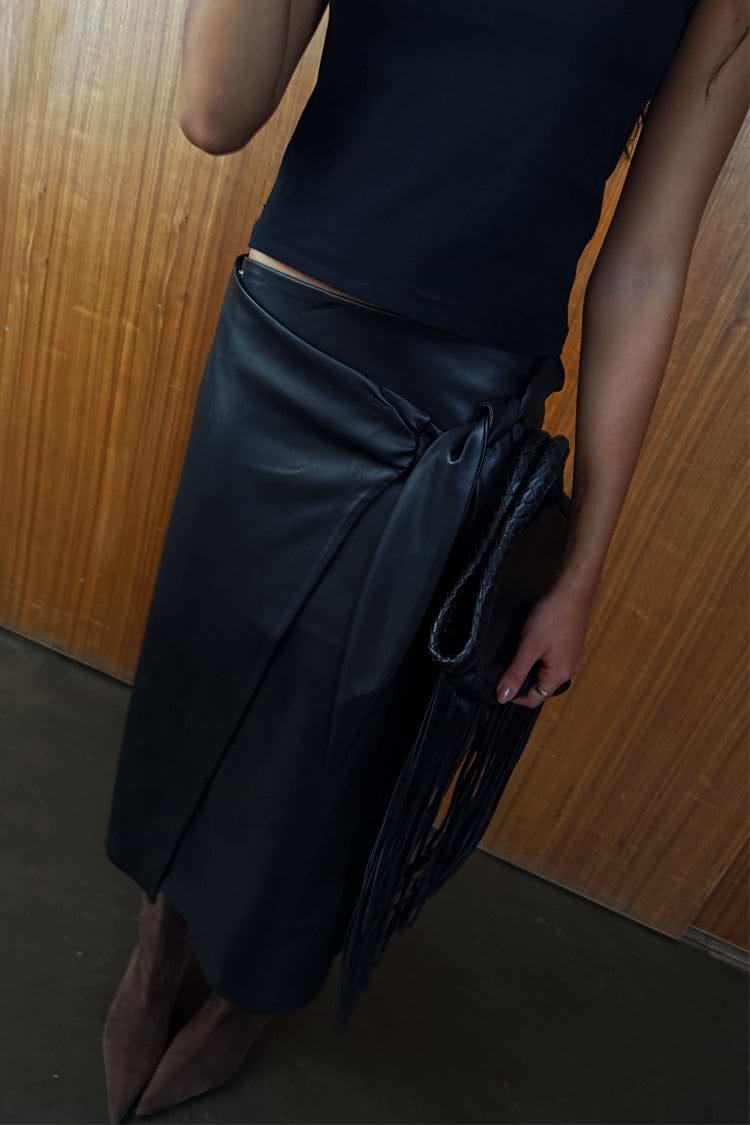 Black vegan leather wrap skirt with a tulip tie detail, styled with a black top and fringe bag.