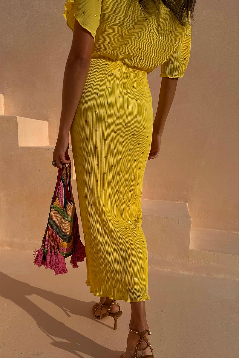 Sunshine Tilly Dress in yellow plissé with gold flecks and lettuce hem, held with a colourful beaded bag.