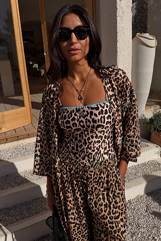 Leopard print bandeau swimsuit with blue whipstitch trim, matching balloon trousers and shirt in a vacation setting.