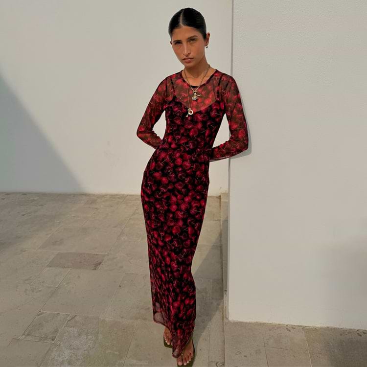 Red digital cherry print Mesh Soho Dress with long sleeves, designed in London and worn by a model against a wall.