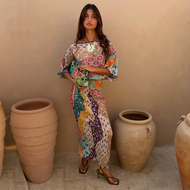 Pastel Morocco Tilly Dress with metallic flecks and sun motifs, styled with a matching clutch beside large clay pots.