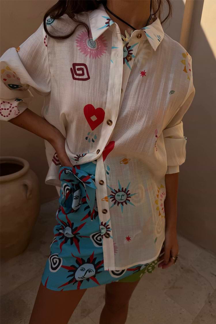 A Morocco Mini Wrap Skirt with blue sun prints layered under a white patterned button-down shirt.