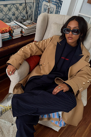 Navy Book The Flight Jumper with red text, layered with a tan studded trench and pinstripe trousers.