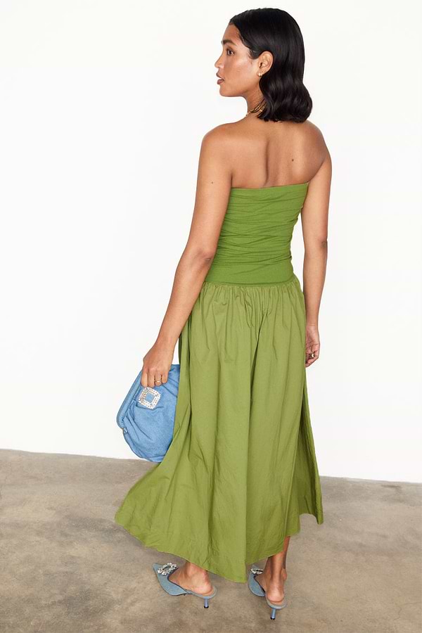 Olive Lola Mid-axi Dress with a ruched strapless top and flowy green cotton skirt, styled with a blue clutch.