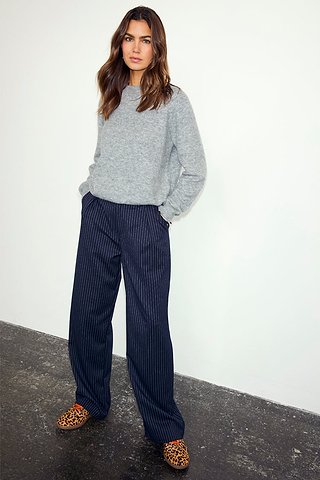 Navy Pinstripe Arden Trousers in a wide-leg fit, styled with a grey knitted jumper and leopard print shoes.
