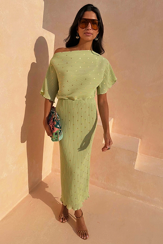 Pistachio Tilly Dress in green plisse with gold flecks and a lettuce hem, styled off-the-shoulder on stairs.