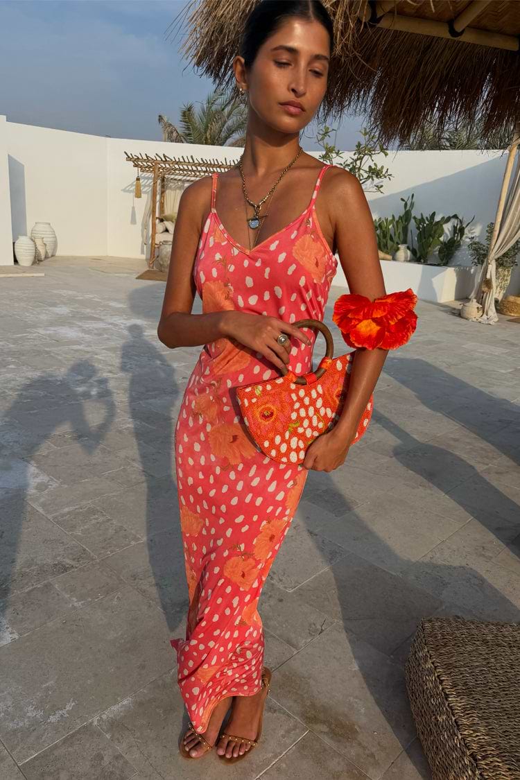 Coral Fawn Poppy Aria dress in pink with orange poppy motifs and white dots, styled with a matching beaded bag.