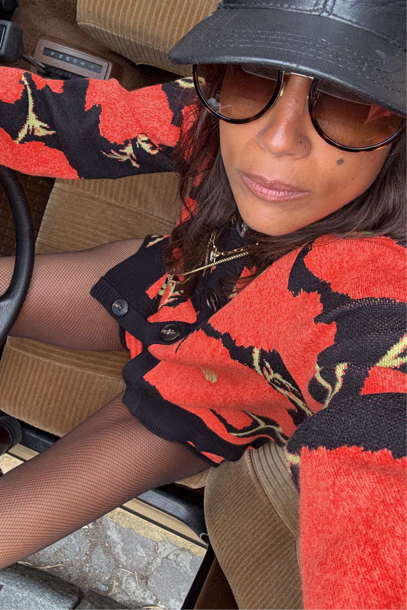 Black Poppy Cardigan with a bold red floral print, styled with fishnet tights and a cap in a vintage car.