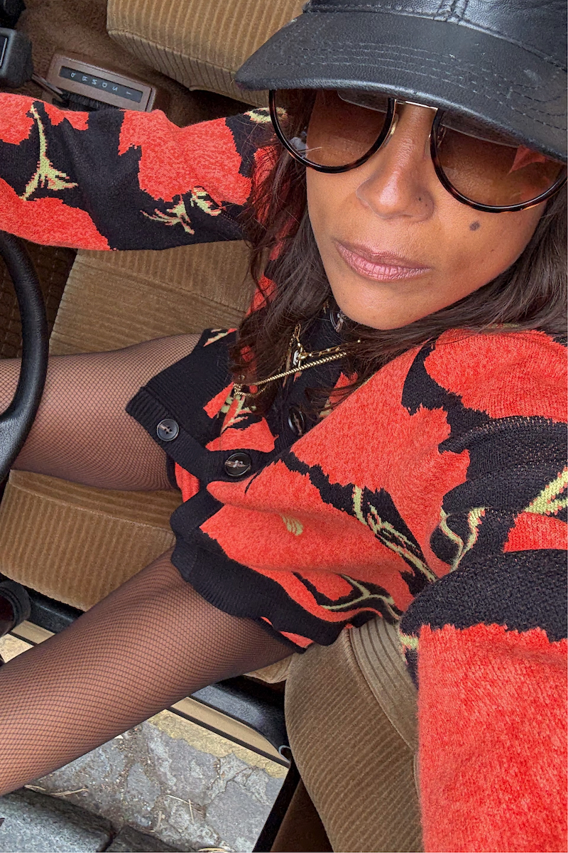 Black Poppy Cardigan with a bold red floral print, styled with fishnet tights and a cap in a vintage car.