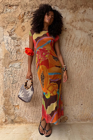 Rio Mesh Dress with fruit motifs and colour blocks in mesh, styled for a vacation against a stone wall.