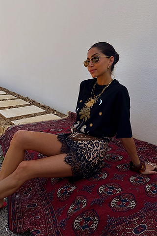 Iconic black Running Wilder T-shirt in cotton with a sun graphic, styled with a leopard print lace skirt on a red rug.