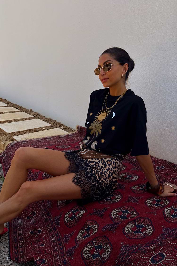 Iconic black Running Wilder T-shirt in cotton with a sun graphic, styled with a leopard print lace skirt on a red rug.