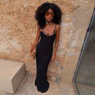 Black Sapna Dress with Ring Detail styled as a maxi dress against a stone wall for a vacation look.
