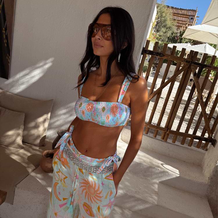 Blue Dreamer Shirred Bandeau Top with a sun and heart print, styled with matching trousers in a holiday setting.