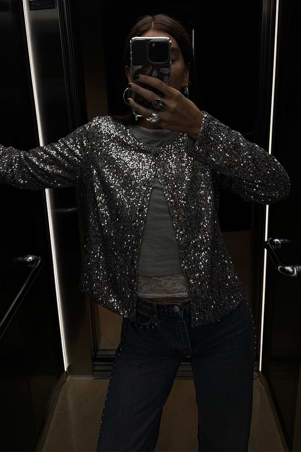 Gunmetal Alexa Sequin Cardigan in a structured silhouette, styled over a grey top and jeans for a party-ready look.