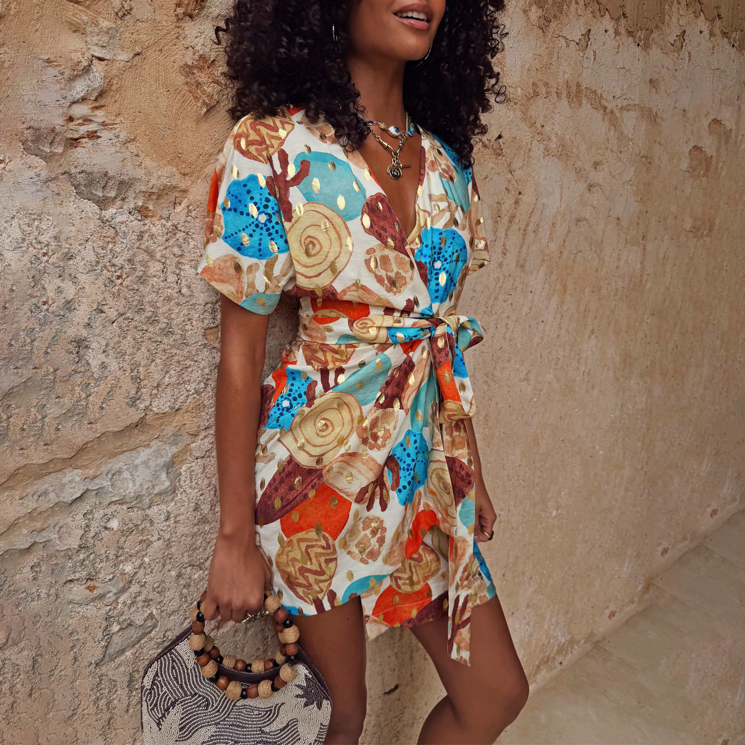 Shell Mini Wrap Dress in a multi-colour abstract shell print with metallic gold accents, flutter sleeves and tie waist.