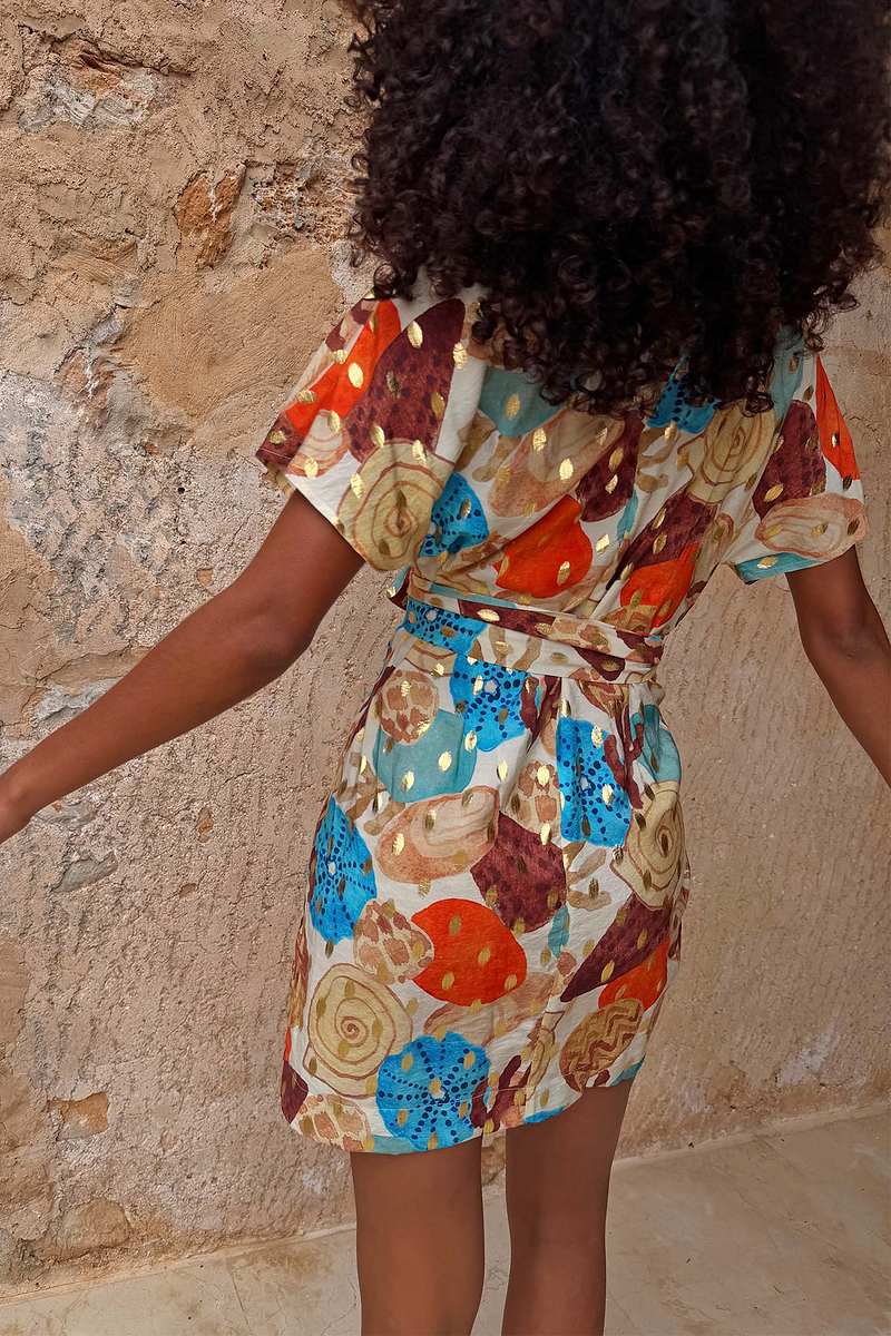 Shell Mini Wrap Dress in an abstract shell print with gold metallic detailing and flutter sleeves, seen from the back.