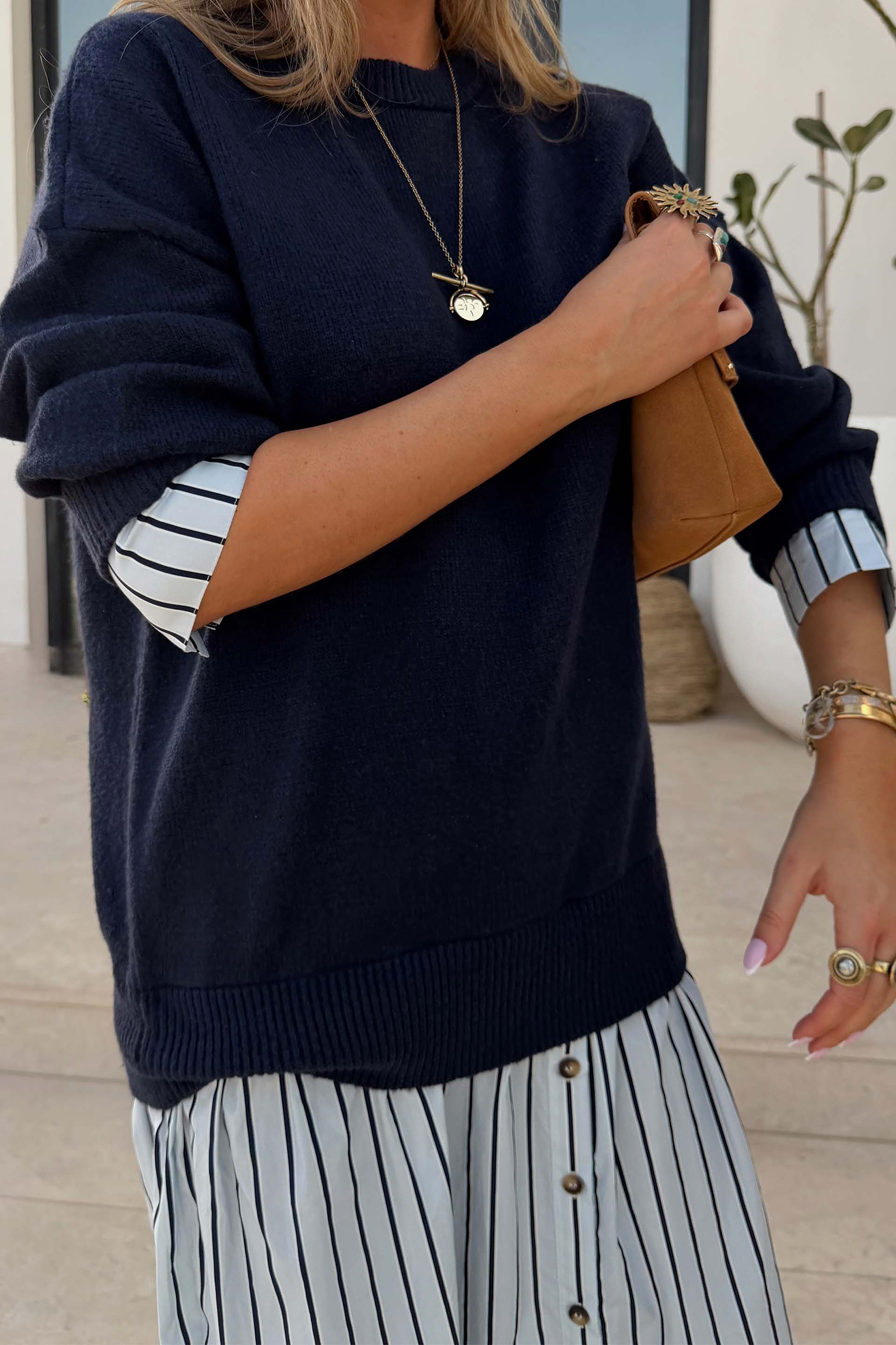 Navy knit jumper dress with a blue striped cotton skirt and layered cuffs, styled with a tan bag.