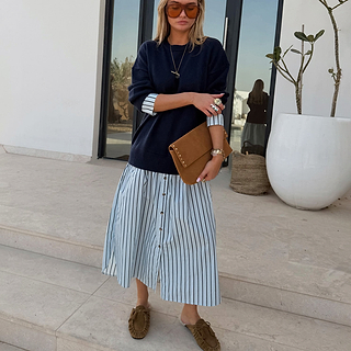 Navy Knit Jumper Dress with a blue stripe cotton skirt, styled with a tan suede clutch for a casual London look.