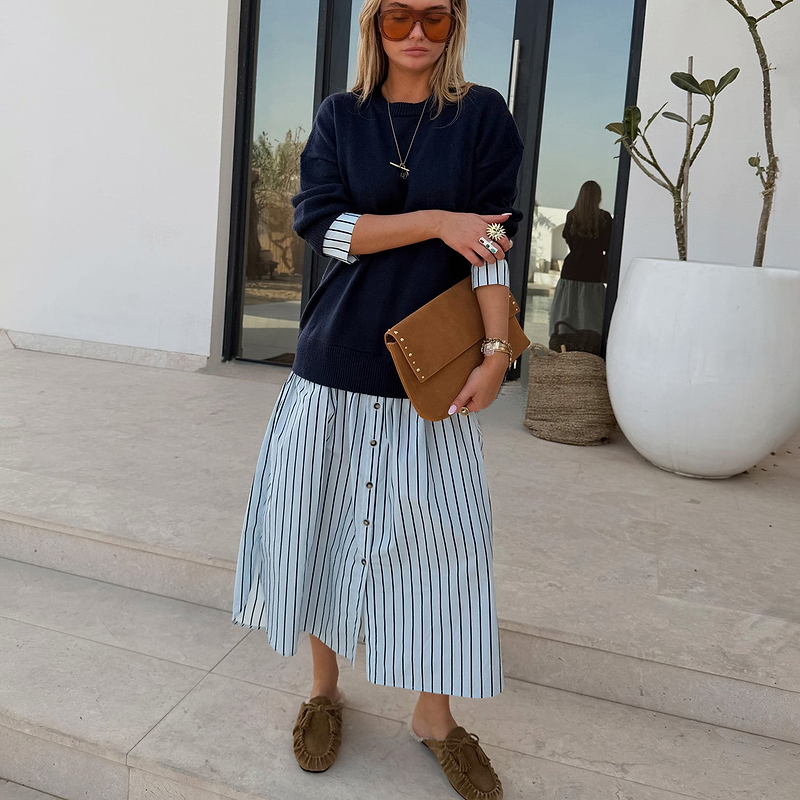 Navy Knit Jumper Dress with a blue stripe cotton skirt, styled with a tan suede clutch for a casual London look.