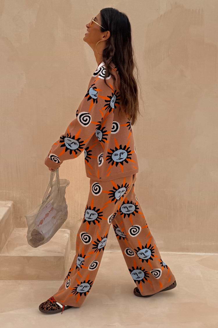 Tan Sun Trousers and matching knit jumper co-ord with sun and swirl motifs, walking on stone steps.