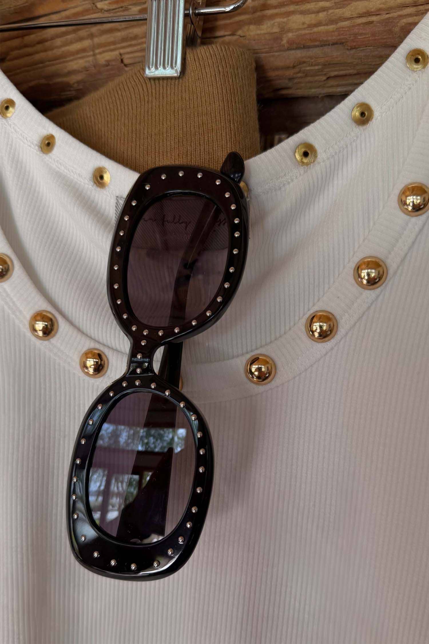 Black Studded Acetate Sunglasses with silver studs and dark lenses, hooked onto a white ribbed top.
