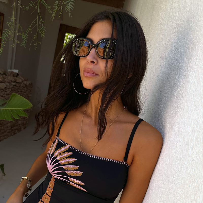 Black acetate sunglasses with silver studs and tinted lenses, worn with a palm tree print swimsuit.