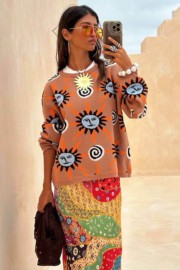 Tan Sun Copenhagen Jumper in a tan knit with hand-painted sun motifs, styled with a colourful patterned skirt.