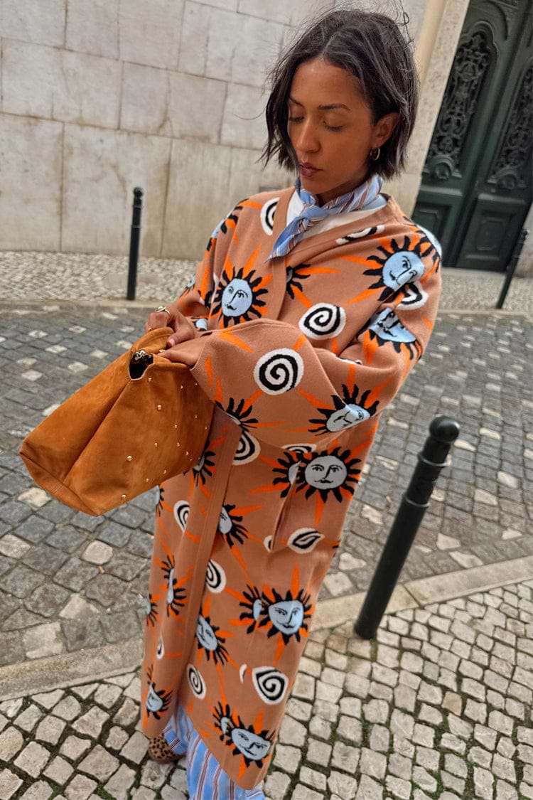 Tan Sun Cardigan with hand-painted sun motifs and dropped shoulders, styled on a cobblestone street.