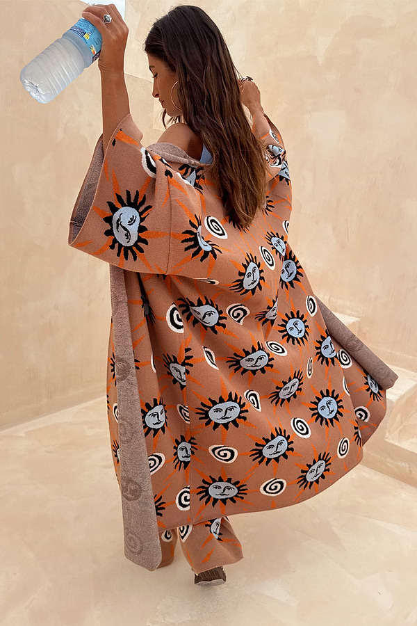 Oversized Tan Sun Cardigan featuring hand-painted Mediterranean sun motifs and wide sleeves in an outdoor setting.