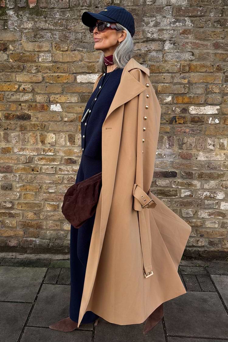 Tan Trench Coat with gold studs on the sleeve, styled with a navy cap and burgundy neck scarf.