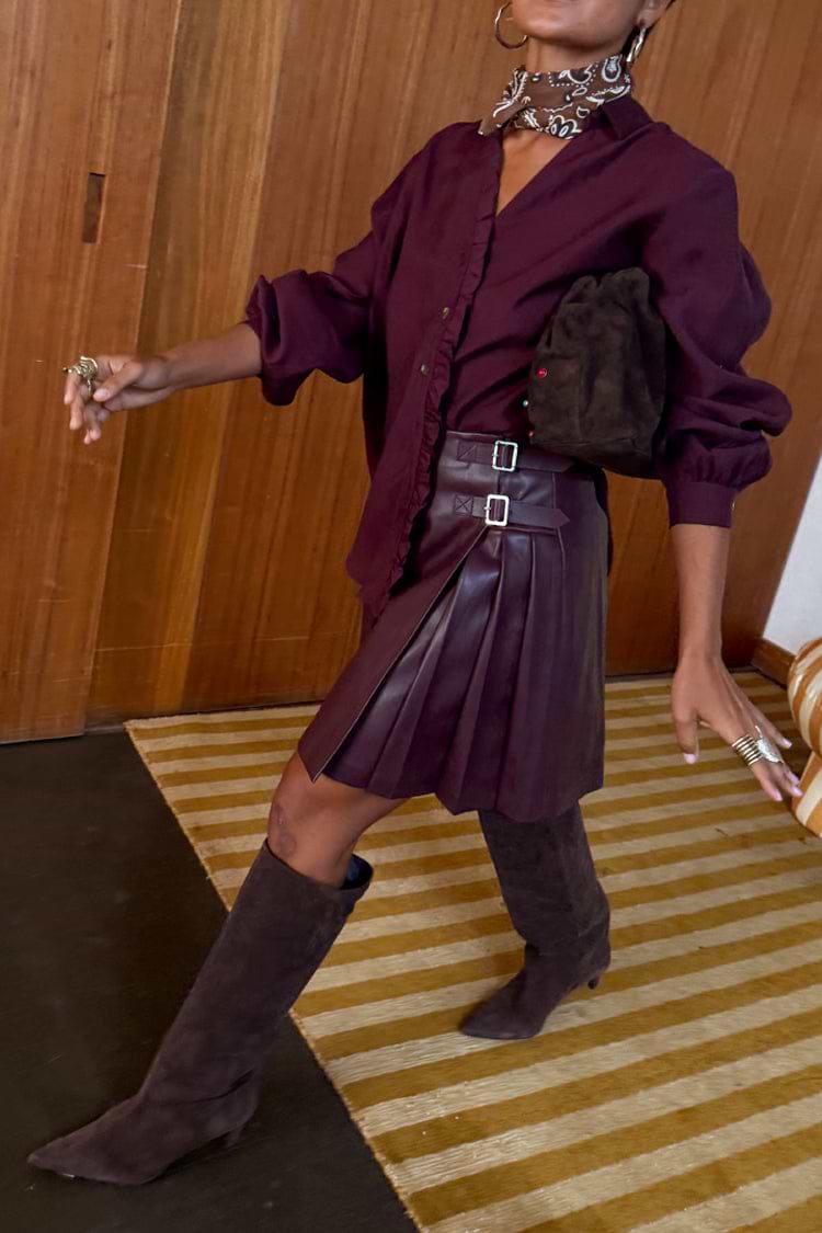 Burgundy vegan leather mini kilt skirt with side pleats and buckle details, styled with a matching wine shirt and boots.