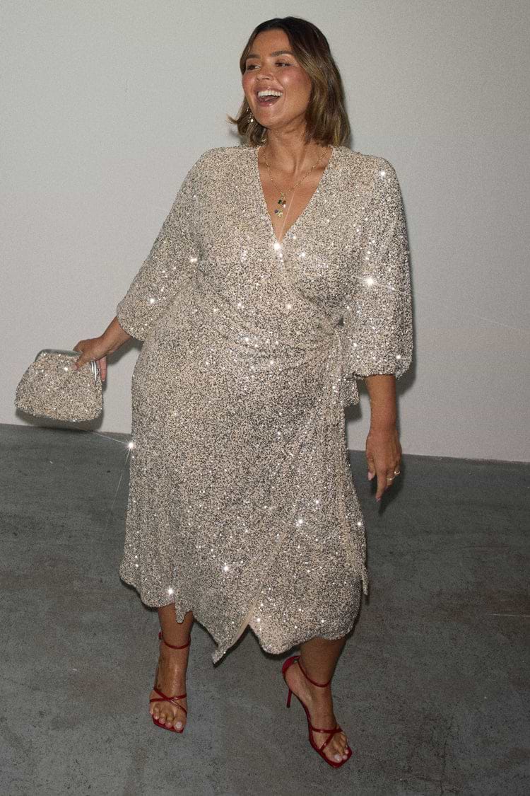 Silver Sequin Kira Wrap Dress with a tie fastening, styled with red heels and shown in UK size 18 for inclusive sizing.