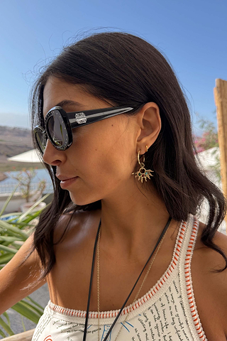 Black Studded Acetate Sunglasses with silver detailing and branding, worn by a model in an outdoor vacation setting.