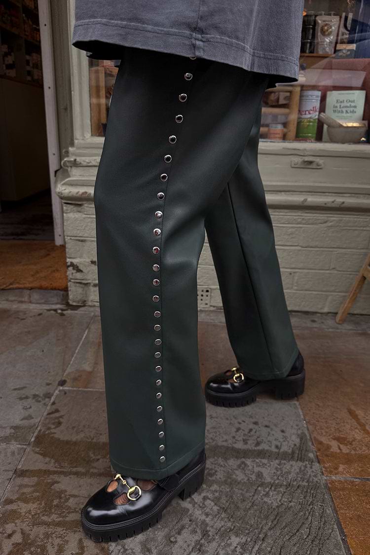 Bottle green vegan leather trousers with silver side studs, styled with chunky loafers in a street style setting.
