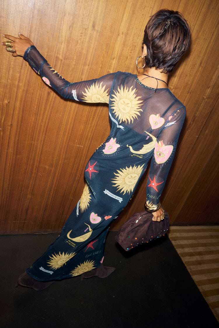 Black Mystical Mesh Dress featuring celestial sun and heart prints, styled with a slip against a wooden wall.