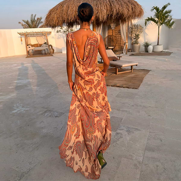 Peach Paisley Ava Dress with a low cowl back and bias-cut maxi silhouette, styled in an outdoor vacation setting.