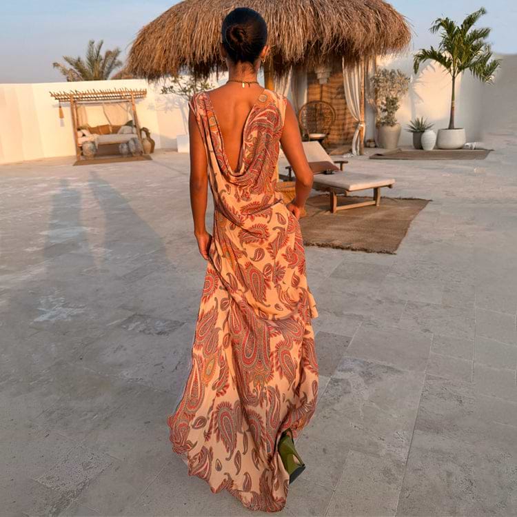 Peach Paisley Ava Dress with a low cowl back and bias-cut maxi silhouette, styled in an outdoor vacation setting.