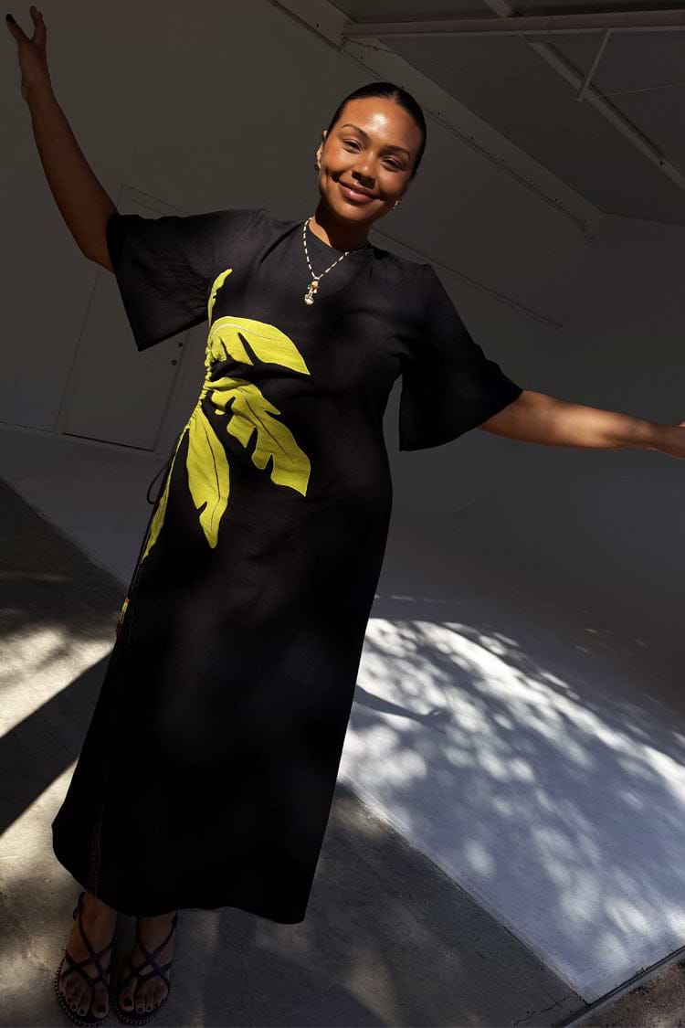 Black Palm Riviera maxi dress featuring a yellow palm motif and side waist cut-out detail.