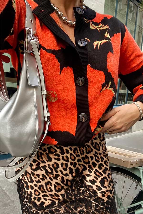 Black Poppy Cardigan with a bold poppy print and button-up front, styled with a leopard print skirt and silver bag.