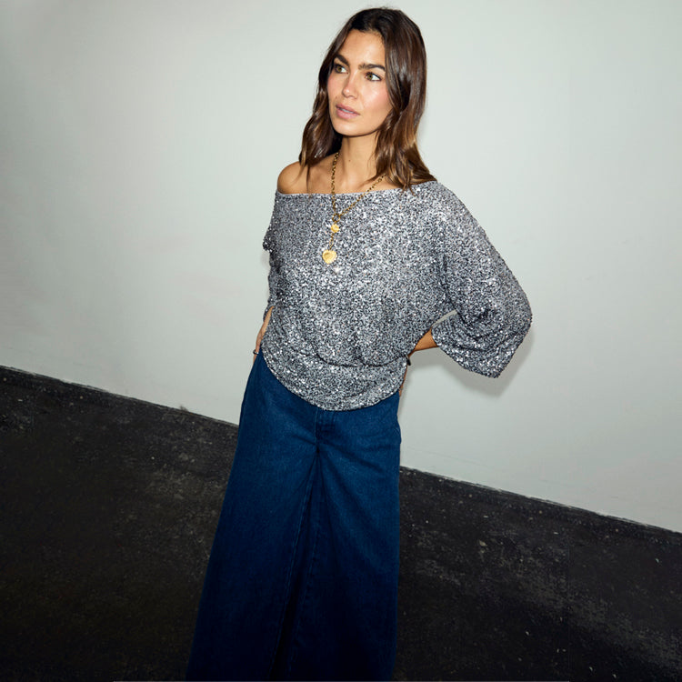Gunmetal Sequin Tilly Top styled off-the-shoulder with dark denim wide-leg jeans on a model.