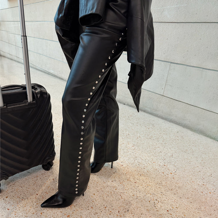 Black vegan leather trousers with silver stud detailing, styled with pointed boots and a black suitcase.