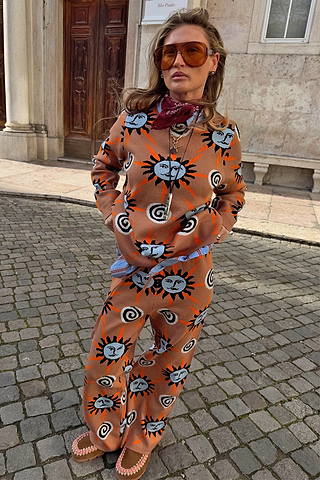 Tan Sun knit co-ord with sun and swirl motifs, styled with a bandana and sunglasses on a cobbled street.