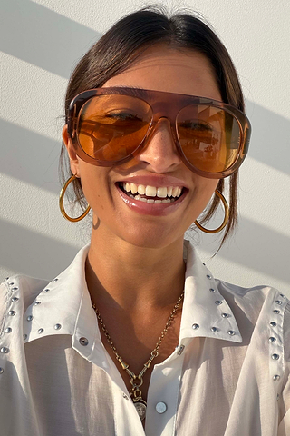 Orange Acetate Visor Sunglasses on a smiling model with 70s-inspired tinted lenses and gold hoop earrings.